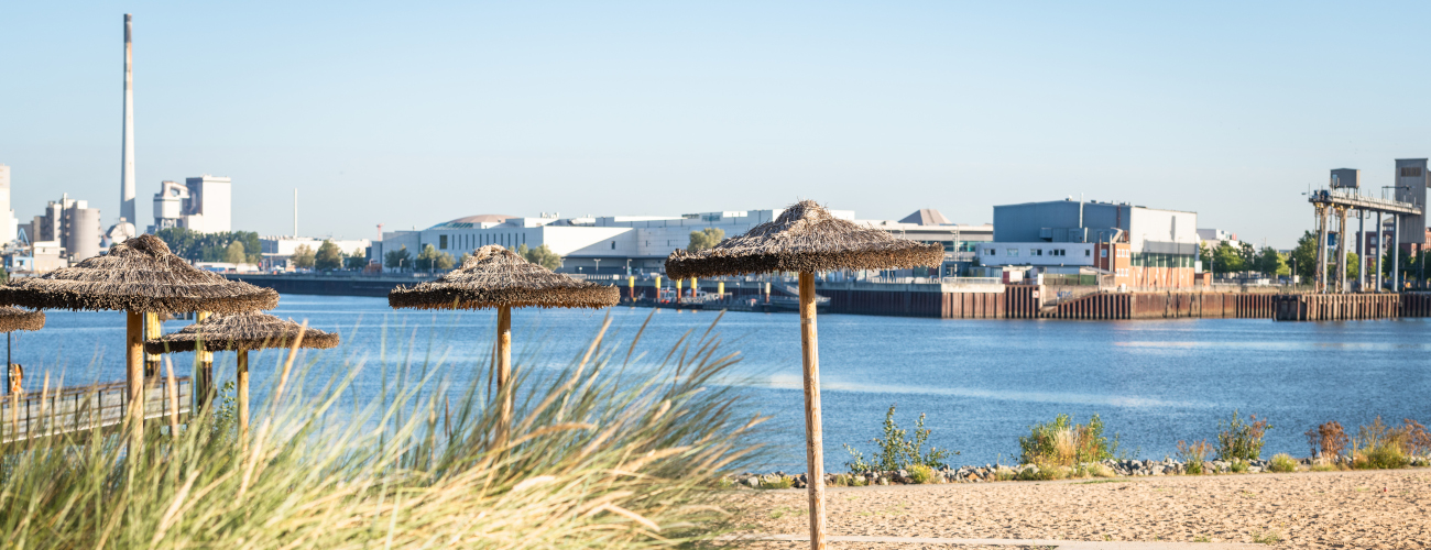 Waller Sand mit Strohschirmen und Bootsanleger mit Blick auf Industriegebäude - Quelle: WFB/Melanka Helms-Jacobs