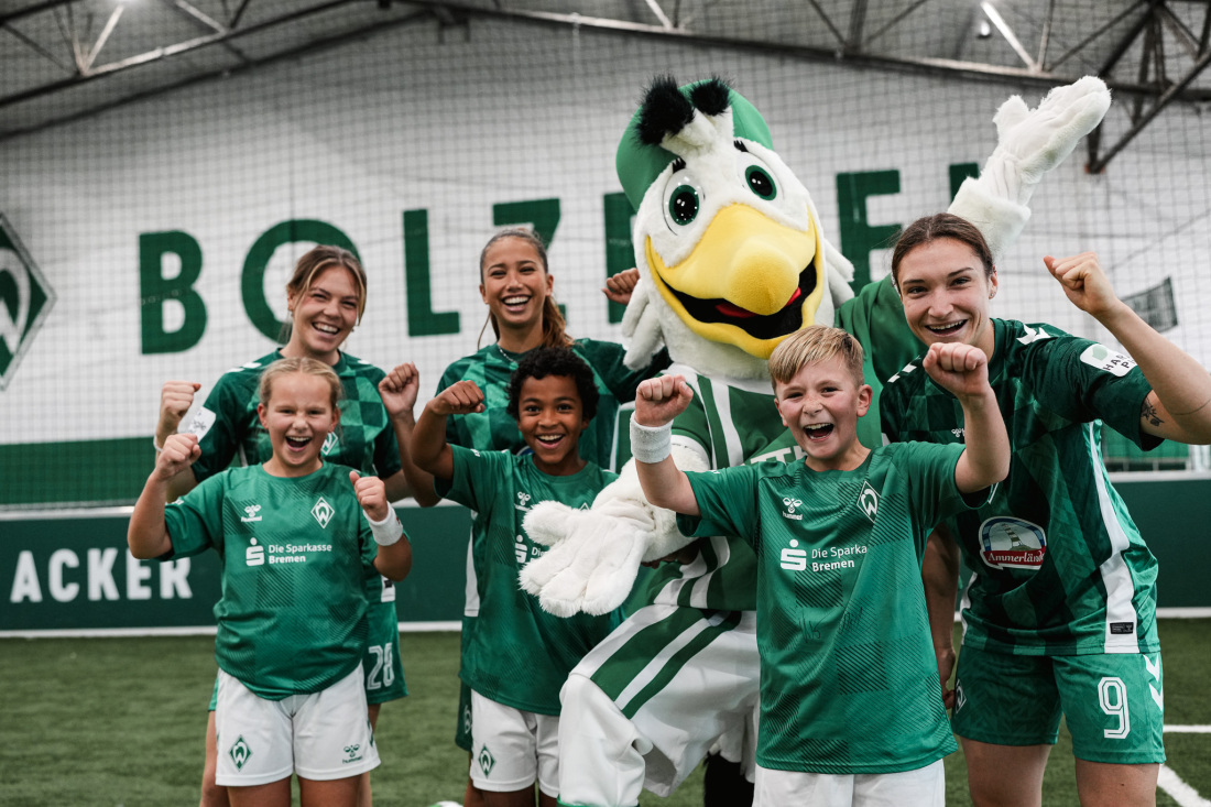 Jubelnde Kinder stehen um das Möwen-Maskottchen der Bolzerei herum und tragen Fußballkleidung.