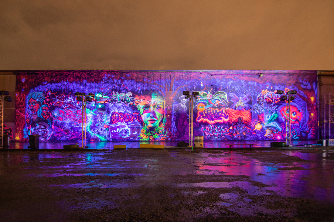 Eine mit Schwarzlicht beleuchtete Fassade wird zum Riesenkunstwerk beim Hidden Treasure Urban Art Festival.