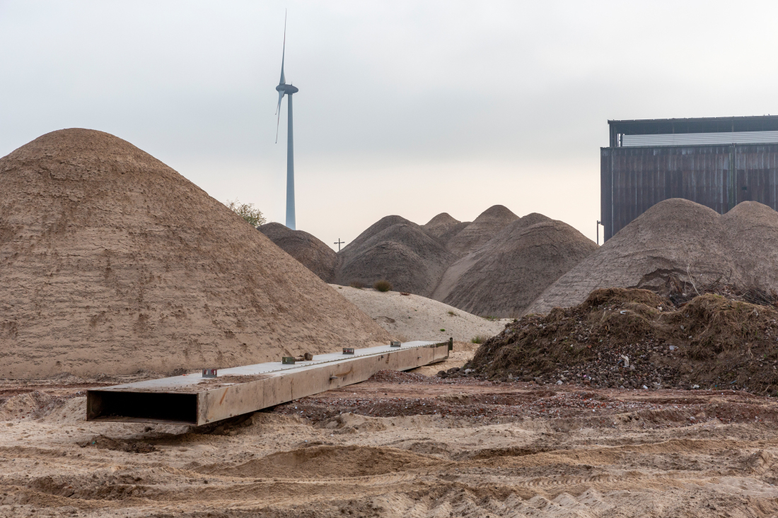 Ein Stahlträger führt den Blick auf die großen Erdhügel einer Baustelle