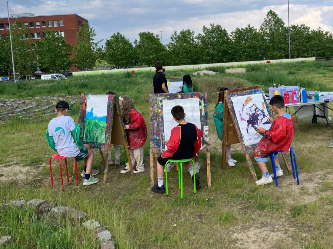 Eine Gruppe von Kinder sitzt auf der Überseewiese, alle haben eine Staffelei vor sich und malen Eine Gruppe von Kinder sitzt auf der Überseewiese, alle haben eine Staffelei vor sich und malen
