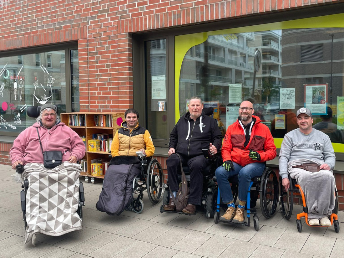 Fünf Männer im Rollstuhl sitzen in warme Kleidung gehüllt vor der Fassade des Quartierstreffs in der Überseestadt Fünf Männer im Rollstuhl sitzen in warme Kleidung gehüllt vor der Fassade des Quartierstreffs in der Überseestadt