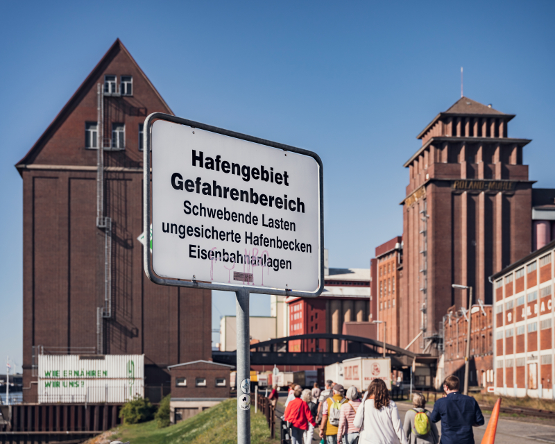 Die Besucherinen und Besucher laufen über das Hafengelände in der Nähe des Holz- und Fabrikenhafens Die Besucherinen und Besucher laufen über das Hafengelände in der Nähe des Holz- und Fabrikenhafens