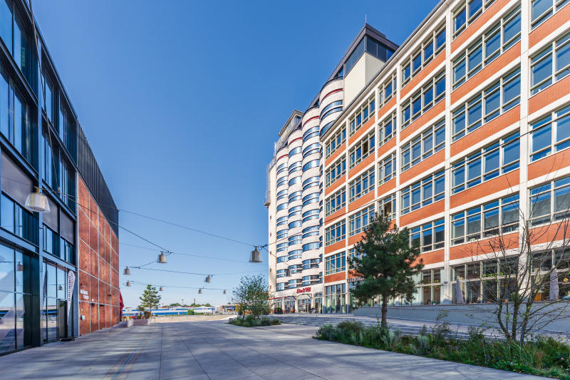 Der Blick ist Richtung Weser gerichtet. Zwischen zwei großen, neu gestalteten Gebäuden mit vielen Fenstern verläuft eine moderne Straße. Am Ende der Straße ist Wasser zu sehen. Der Himmel ist klar und blau, die Szene wirkt urban und aufgeräumt.